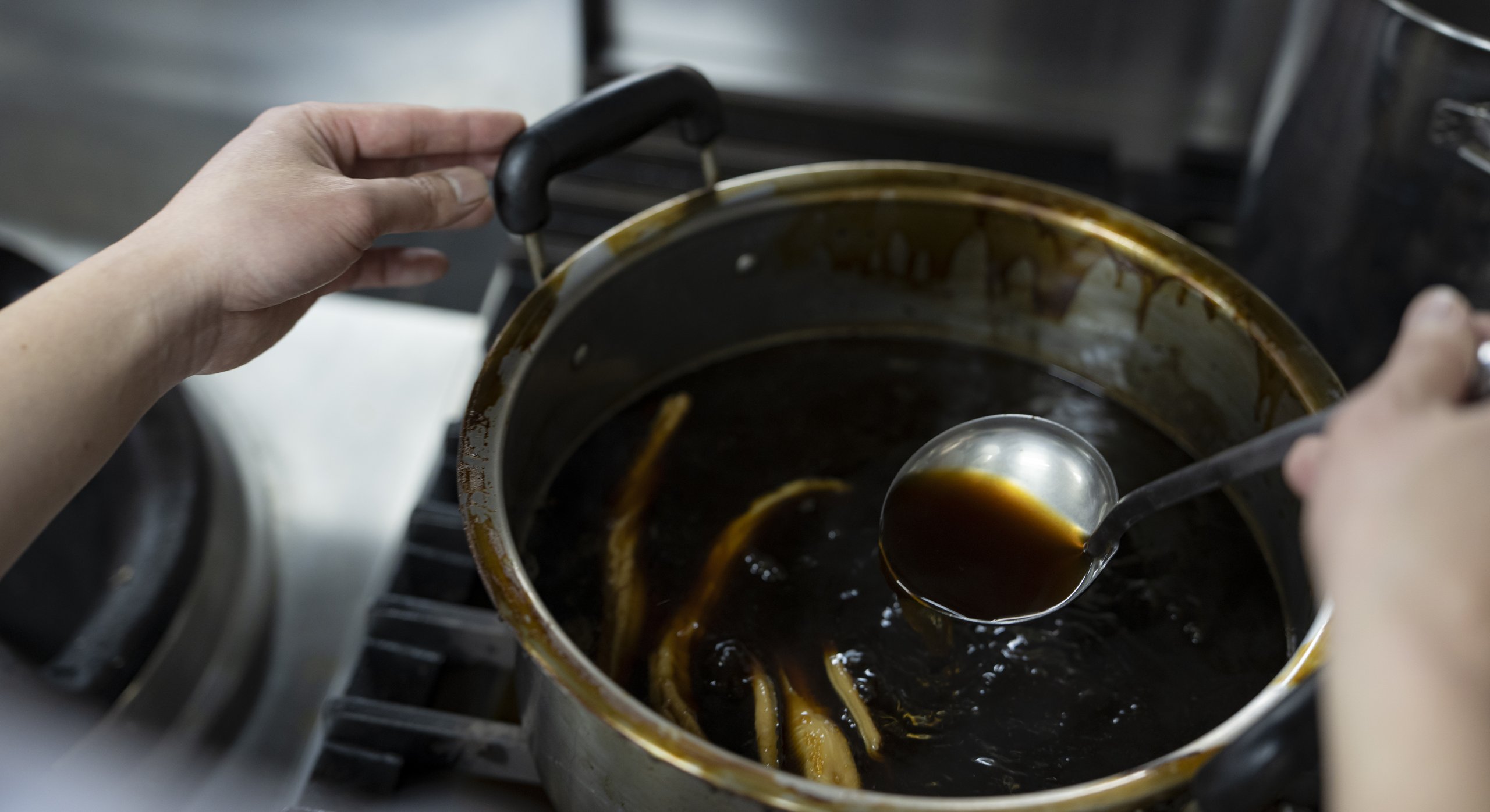 鍋の煮汁をおたまですくう手元